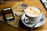 Tasse Kaffee mit Handy und Kopfhörern daneben