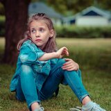 Kind sitzt auf einer Wiese und schaut zur Seite 