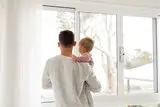 Mann mit Kind im Arm vor dem Fenster